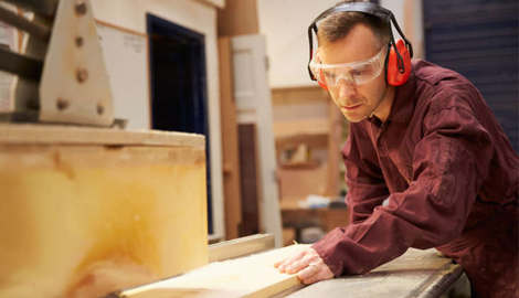 A man wearing a hard hat and safety glasses is focused on working with a piece of wood in a construction of portable office containers - office and dry containers