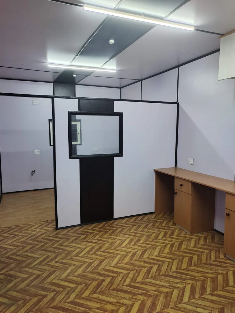 A steel prefab office container with a desk and a wall that has a door, providing a practical and orderly workspace - office and dry containers